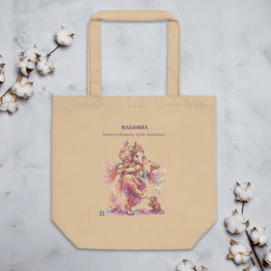 Op de afbeelding: Een beige draagtas met een kleurrijke illustratie van de godheid Ganesha die danst met een kleine muis. De tekst Ganesha en Remove obstacles, invite abundance staat erboven gedrukt, met een kleine groene letter D in de hoek.