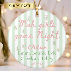 May include: A round ceramic ornament featuring a light green and white vertical striped background. The text reads Mah girls game Night crew, followed by the names Emma, Bonnie, Evie, Charlotte, Libby, and est 2026. Small mahjong tile icons are scattered.