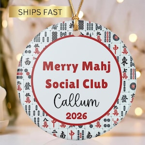 May include: A round ceramic ornament featuring a pattern of mahjong tiles in black, red, and white. The centre has a white circle with a red border containing the red text Merry Mahj Social Club, the black name Callum, and the red year 2026.
