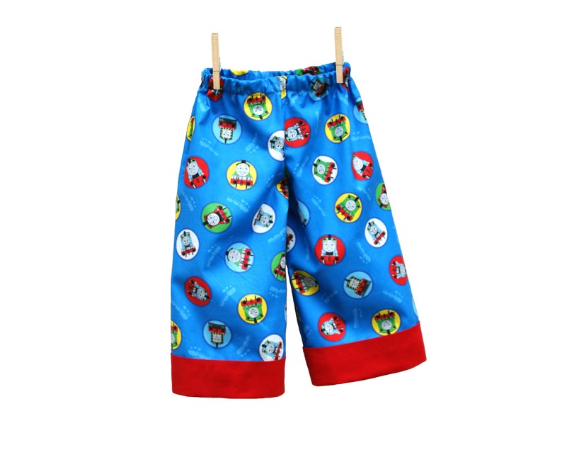 May include: Blue and red children's shorts with a repeating pattern of cartoon train characters in circles.