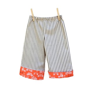 May include: White and black striped pants with orange trim featuring a bicycle print. The pants are hanging on a clothesline with wooden clothespins.