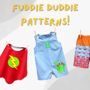May include: Three different clothing items for children, hanging on a clothesline. A red cape with a yellow lightning bolt, a blue and white gingham overall with a green dinosaur applique, and orange and red patterned shorts with a crab design.