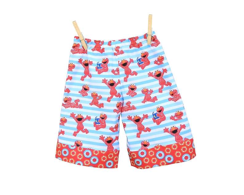 May include: Blue and white striped shorts with a red Elmo print. The shorts have a red and orange trim with a circle pattern.