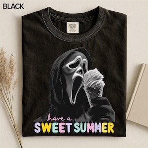 Op de afbeelding: Een zwart t-shirt met een afbeelding van een figuur met een capuchon en een wit masker die een hoorntje ijs vasthoudt. Onder de afbeelding staat de tekst "have a SWEET SUMMER" in kleurrijke, afgeronde letters. Comfort Colors label aanwezig.