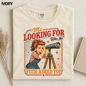 Könnte beinhalten: Ein elfenbeinfarbenes T-Shirt mit einer Grafik im Vintage-Stil, die eine Person mit einem rot gepunkteten Haarband zeigt, die durch ein Teleskop schaut. Der Text lautet "Me LOOKING FOR Who the FUCK ASKED YOU" in roter und blauer Schrift auf gepunktetem Grund.