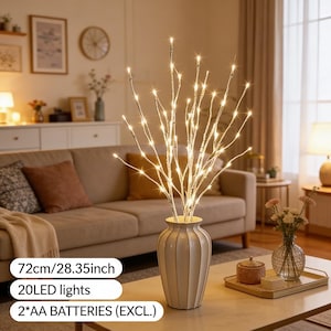May include: A white ceramic vase holding illuminated faux branches with 20 LED lights. The branches are 72cm tall and require 2 AA batteries. The vase is on a marble-topped table in a living room.