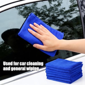 Può includere: Un panno in microfibra blu pulisce un finestrino dell'auto. È visibile una pila di panni blu. Il testo "Used for car cleaning and general wiping" è incluso.