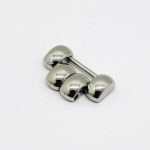 May include: A silver-toned metal watch band link extension piece consisting of four rounded, polished segments connected by a thin horizontal metal pin. The component features a smooth, reflective surface and a curved design for a watch bracelet.