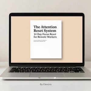 May include: A laptop displays a white book cover with the title "The Attention Reset System" and the subtitle "14 Day Focus Reset for Remote Workers." A coffee mug, plant, notebook, pen, and phone are on the desk.
