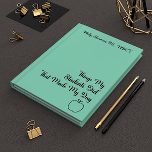 Op de afbeelding: Een mintgroen notitieboek met harde kaft en zwarte tekst met de tekst Philip Sherman 38, NBCT en Things My Students Did That Made My Day, voorzien van een eenvoudige lijntekening van een appel. Het notitieboek ligt naast een gouden en zwart potlood.