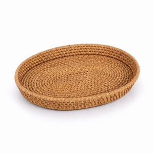 May include: An oval-shaped tray crafted from woven light brown rattan. The tray features a continuous, tightly woven base and raised sides with a consistent, textured pattern throughout the entire structure, presenting a natural tan color.