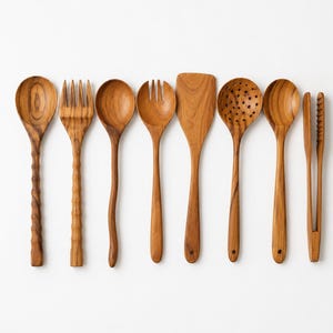 Könnte beinhalten: Ein Set aus acht hellbraunen Küchenutensilien aus Holz, bestehend aus einem Löffel, einer Gabel, einem runden Löffel, einer Salatgabel, einem flachen Pfannenwender, einem Schaumlöffel, einem Rührlöffel und einer Holzzange mit sichtbarer Maserung.