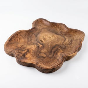 May include: A brown wooden serving tray with an irregular, organic shape and a natural wood grain pattern. The surface features a central knot and swirling dark brown rings that follow the contours of the wood, creating a textured appearance.