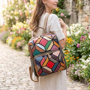 May include: A colorful leather backpack with a geometric patchwork design. The backpack features a variety of colors including red, blue, green, and brown. It has a top handle, adjustable straps, and multiple zippered compartments.