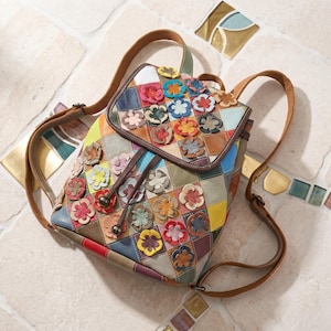 Puede incluir: Mochila de cuero patchwork multicolor con cierre de solapa y cordón. La mochila presenta una variedad de colores y está decorada con aplicaciones de flores en 3D. Las correas y el asa son marrones.