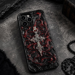 Pode incluir: Uma capa de smartphone preta com um padrão em relevo intrincado de vinhas em vermelho escuro e preto. Um pingente de cruz em tom prateado está fixado na parte superior central da capa, repousando sobre a superfície texturizada.