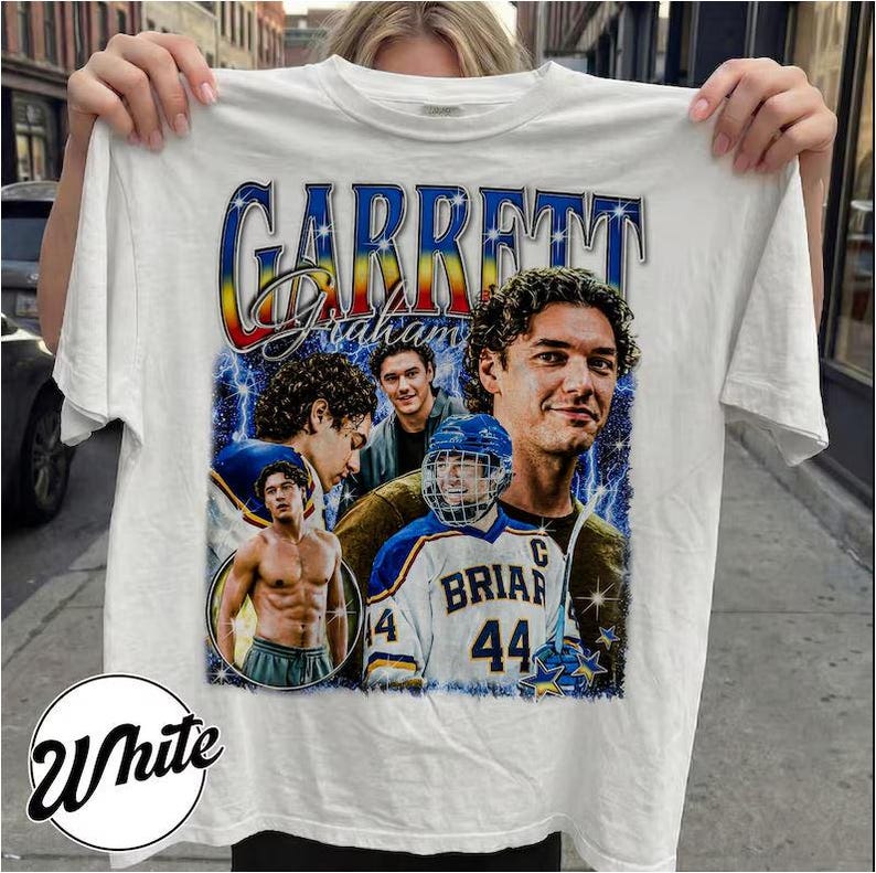 May include: White t-shirt featuring a graphic of Garrett Graham with multiple images of him, including one in a hockey uniform. The design includes the name "Garrett Graham" in a stylized font with a blue, yellow, and red gradient.