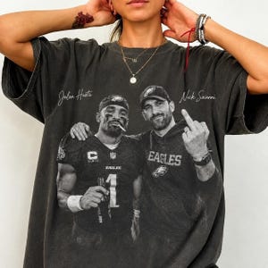 Peut inclure: Un t-shirt gris anthracite à manches courtes avec une impression graphique de style vintage représentant Jalen Hurts et Nick Sirianni. Le texte Jalen Hurts et Nick Sirianni est imprimé au-dessus des personnages. Col rond et coupe décontractée.