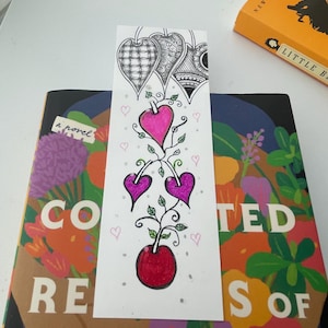 Könnte beinhalten: Ein rechteckiges Lesezeichen aus Papier mit einer handgezeichneten Illustration einer vertikalen Ranke mit drei herzförmigen Früchten in Pink und Lila sowie einer roten runden Frucht an der Basis, gekrönt von drei schwarz-weiß gemusterten Blättern.