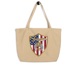 May include: A beige tote bag featuring a central shield emblem. The shield displays the American flag pattern, a horizontal silver scimitar, and a gold pharaoh head icon with a crescent moon and a five-pointed star hanging from the blade.