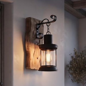 A rustic wood lantern wall sconce by Midnight Beam Co measuring 330mm tall and 150mm wide, mounted on a cream wall, featuring a solid reclaimed wood backing, a powder-coated black steel lantern, and a glowing Edison bulb inside a clear glass enclosure.