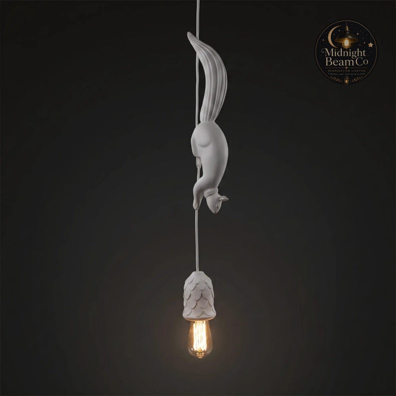 May include: A white squirrel-shaped pendant light fixture. The squirrel is suspended from a cord, with a decorative shade and a vintage-style Edison bulb. The light fixture is against a dark background.