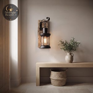 A rustic reclaimed wood wall lamp with a hanging black lantern, mounted on a neutral wall, showing the natural wood grain texture of the backing panel, the copper nail accents, and the warm inviting glow cast by the Edison bulb.