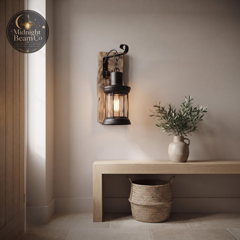 A rustic reclaimed wood wall lamp with a hanging black lantern, mounted on a neutral wall, showing the natural wood grain texture of the backing panel, the copper nail accents, and the warm inviting glow cast by the Edison bulb.