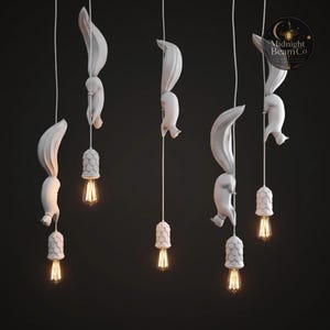A matte white resin squirrel pendant lamp hanging from a white cord against a dark background, showing the lifelike diving squirrel posture with outstretched paws, long tail, and warm Edison filament bulb glowing below.