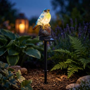 May include: A solar-powered garden stake featuring a bluebird perched on a faux-stone base. The bird has blue and yellow coloring, and the stake is black. The bird is illuminated by a soft light, creating a decorative outdoor accent.