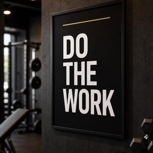 Pode incluir: Um quadro retangular preto numa moldura fina preta com o texto branco DO THE WORK numa fonte sem serifa em negrito, com uma linha horizontal dourada fina acima do texto, exibido numa superfície de parede escura e texturizada.
