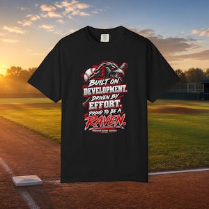 May include: A black short-sleeve t-shirt featuring a graphic of a raven, a baseball, and a bat. The text reads: BUILT ON DEVELOPMENT. DRIVEN BY EFFORT. PROUD TO BE A RAVEN. VANCOUVER RAVENS BASEBALL EST 2024. The design uses white and red lettering.