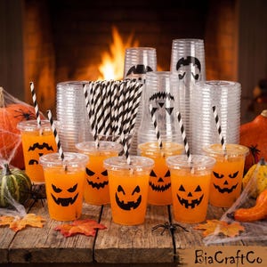 May include: A collection of clear plastic cups filled with orange liquid, each featuring a black jack-o'-lantern face. The set includes black and white striped paper straws and stacks of empty cups with matching designs, all arranged on a wooden surface.