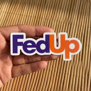 May include: A die-cut vinyl sticker featuring the text FedUp in a bold, sans-serif font. The letters Fed are colored in a deep purple, while the letters Up are in a vibrant orange. The entire word is outlined in a clean white border.