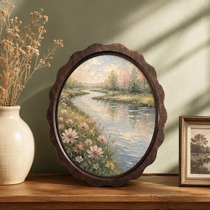 May include: A round, scalloped-edge dark wood frame containing an oil painting of a winding river landscape. The scene features soft pink flowers in the foreground, lush green trees along the banks, and a pale, cloudy sky reflected in the water.