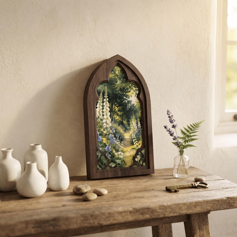 May include: A dark wood gothic arch frame containing a painting of a lush forest path with white foxglove flowers, blue blossoms, and green foliage. The frame is displayed alongside three white ceramic vases, a small glass vase with lavender and fern.