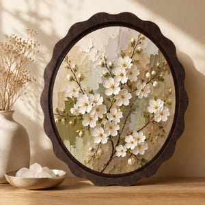 May include: A circular wall art piece featuring a textured impasto painting of white cherry blossoms on a branch. The artwork is encased in a dark brown scalloped wooden frame, showcasing thick paint strokes in shades of cream, beige, and sage green.