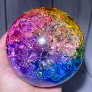 May include: A spherical object with a smooth, clear outer surface and a textured, multi-coloured interior. The internal structure features a vibrant gradient of colours including yellow, pink, purple, and blue, with a crystalline, fractured appearance.