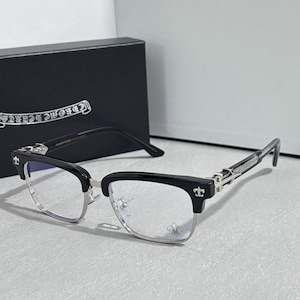 May include: Black and silver-toned eyeglasses with a rectangular frame. The glasses have a silver-toned lower frame and black upper frame. The temples are silver-toned with a decorative design. A black box is in the background.