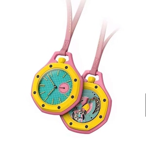 May include: Two octagonal pendant watches with pink frames, yellow bezels, and teal textured dials. One watch features a small circular sub-dial, while the other displays an exposed mechanical movement. Both hang from pink leather straps.