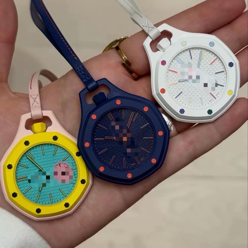 May include: Three octagonal pocket watches with attached straps. One is yellow with a teal face, one is dark blue with a matching face, and one is white with a white face featuring colorful hour markers. Each watch has a textured dial pattern.