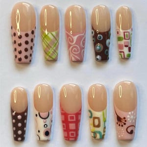 May include: A set of ten press-on nails featuring a nude base with various decorative patterns on the tips. Designs include brown polka dots, green plaid, white swirls, brown circles, geometric squares, pink circles, and floral motifs.