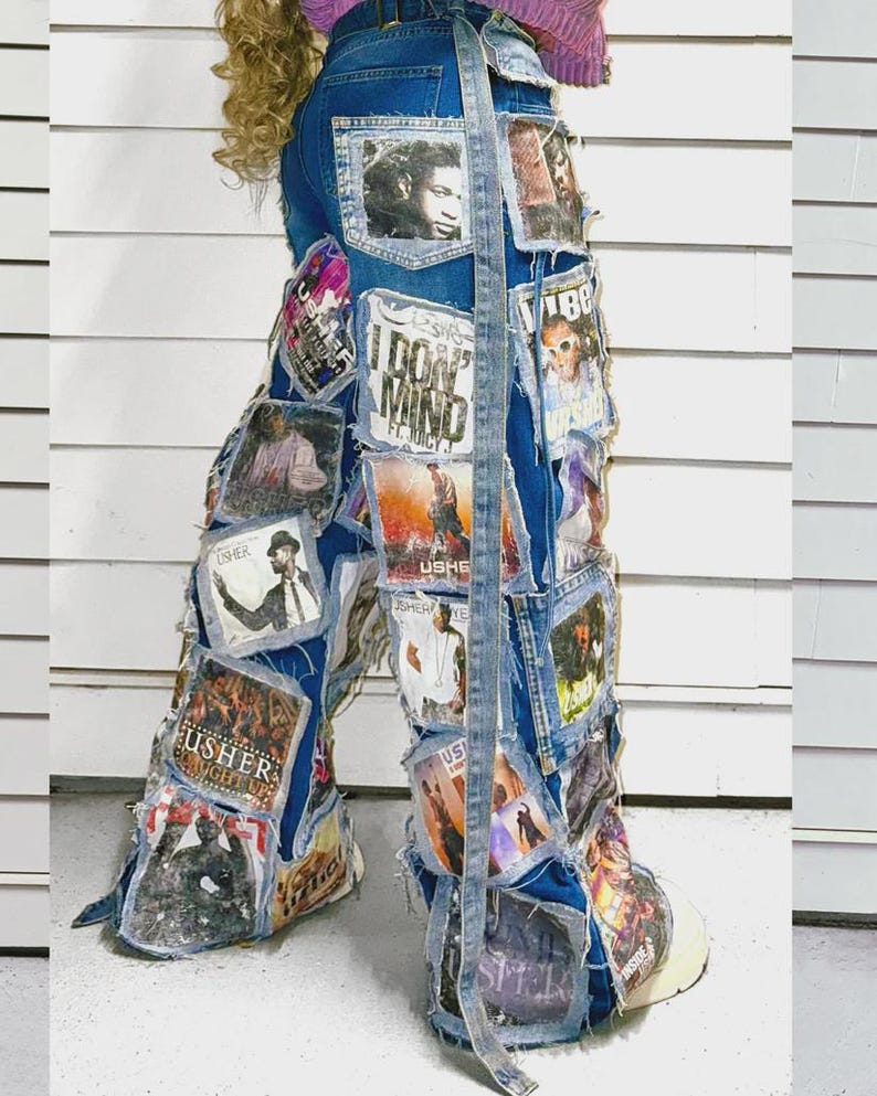Puede incluir: Vaqueros de mezclilla azul con un collage de parches rectangulares con im&aacute;genes impresas y texto, incluido el nombre Usher. Los vaqueros tienen una silueta de pierna ancha, bordes deshilachados en los parches y una tira larga de mezclilla.