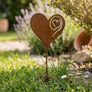 May include: A weathered metal garden stake in the shape of a heart, with a smaller heart design. The stake is made of brown metal and is set in green grass. The heart design has a lighter, golden colour.