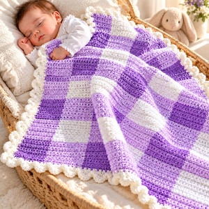 May include: A handmade crochet baby blanket featuring a chequered pattern of alternating white, light purple, and dark purple squares. The blanket is finished with a scalloped white border and is draped over a sleeping infant in a woven basket.
