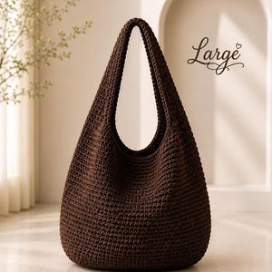 Puede incluir: Un bolso estilo hobo de color marr&oacute;n oscuro confeccionado con un patr&oacute;n de punto de ganchillo denso y texturizado. El bolso cuenta con una sola correa integrada para el hombro y una base redondeada. La palabra Large aparece a la derecha.