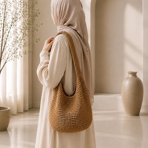 Puede incluir: Un bolso de hombro marr&oacute;n de tama&ntilde;o mediano, estilo hobo, confeccionado con un patr&oacute;n de tejido de ganchillo denso y texturizado. El bolso cuenta con una correa &uacute;nica, ancha e integrada, que descansa sobre el hombro con un punto uniforme.