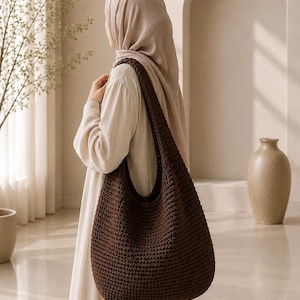 Puede incluir: Un bolso de hombro estilo hobo de color marr&oacute;n oscuro confeccionado en tejido de ganchillo denso y texturizado. El bolso presenta una correa ancha integrada y un cuerpo espacioso y redondeado con un patr&oacute;n de puntos uniforme.