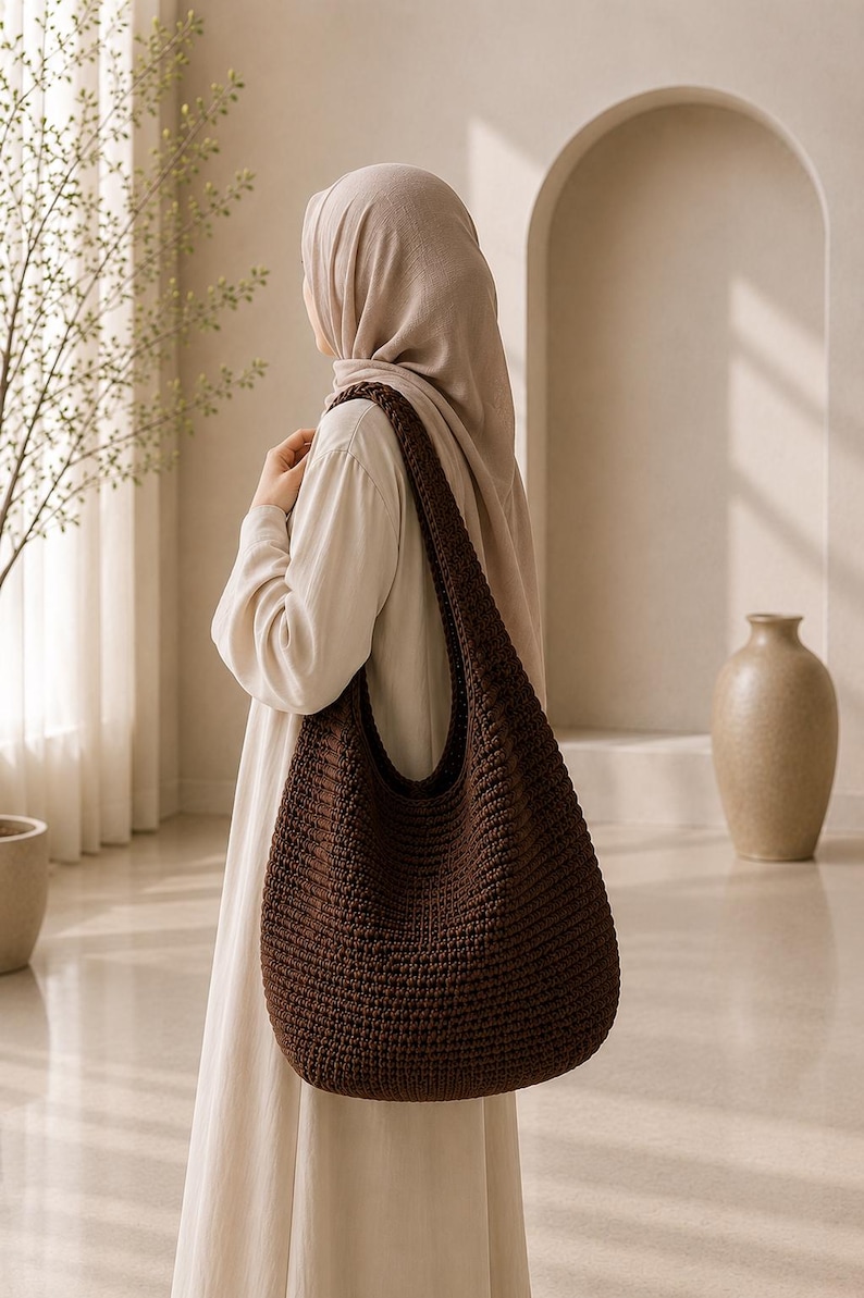 Puede incluir: Un bolso de hombro estilo hobo de color marr&oacute;n oscuro confeccionado en tejido de ganchillo denso y texturizado. El bolso presenta una correa ancha integrada y un cuerpo espacioso y redondeado con un patr&oacute;n de puntos uniforme.