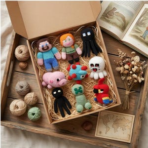 May include: A collection of nine small, handcrafted crochet figures arranged inside a cardboard box filled with straw. The figures include characters with human-like features, a pink pig, a green creature, a red parrot, and black octopus-like shapes.